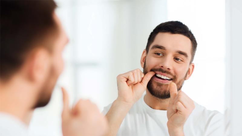 man flossing his teeth in front of a mirror