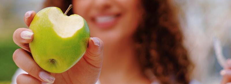 Brunette woman biting or eating a green apple without wearing clear aligners