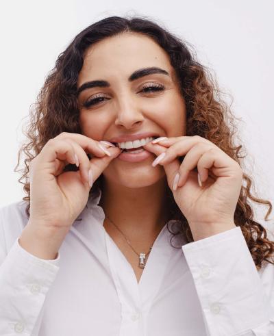 Woman with curly hair, smiling and putting a clear aligner in her upper teeth.