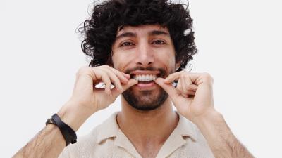 Man with curly brown heair putting invisible aligners in teeth