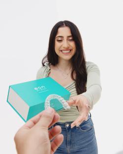 Brunette woman smiling and receiving a set of clear aligners from Eon Aliger 