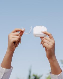 Hands holding invisible aligners and its case with a sky blue background